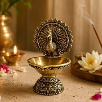 Decorative brass oil lamp with peacock design on a table with flowers and candles.