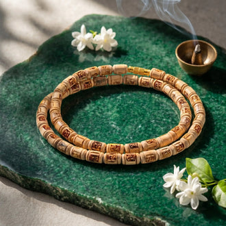 Wooden beaded bracelet on a green stone surface with incense and flowers