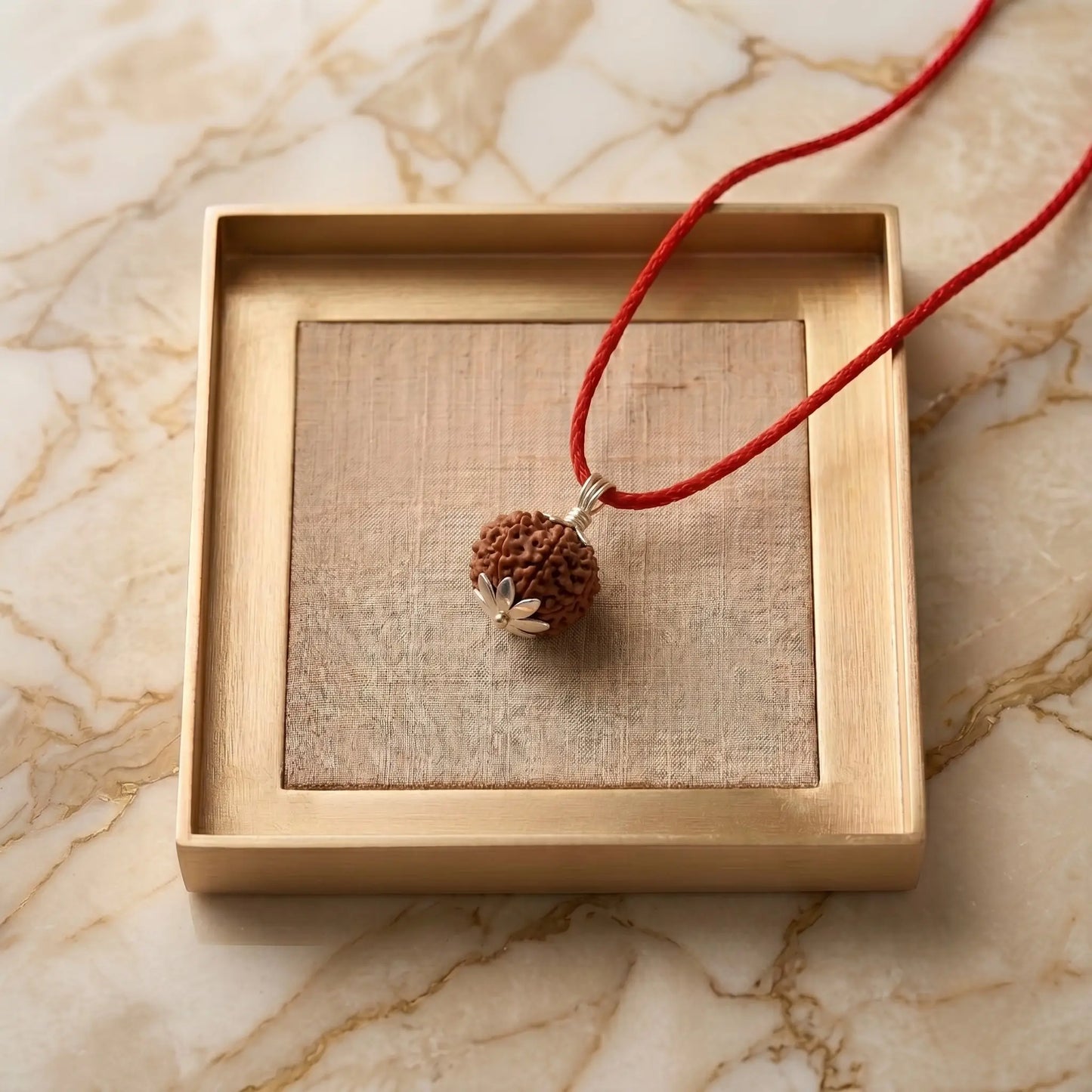 Silver-capped Rudraksha pendant on a red thread cord, displayed on a stone slab with fresh flowers