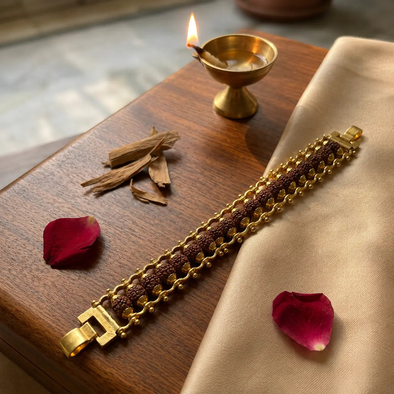Gold plated Rudraksha bracelet on a wooden surface with a lit candle and rose petals