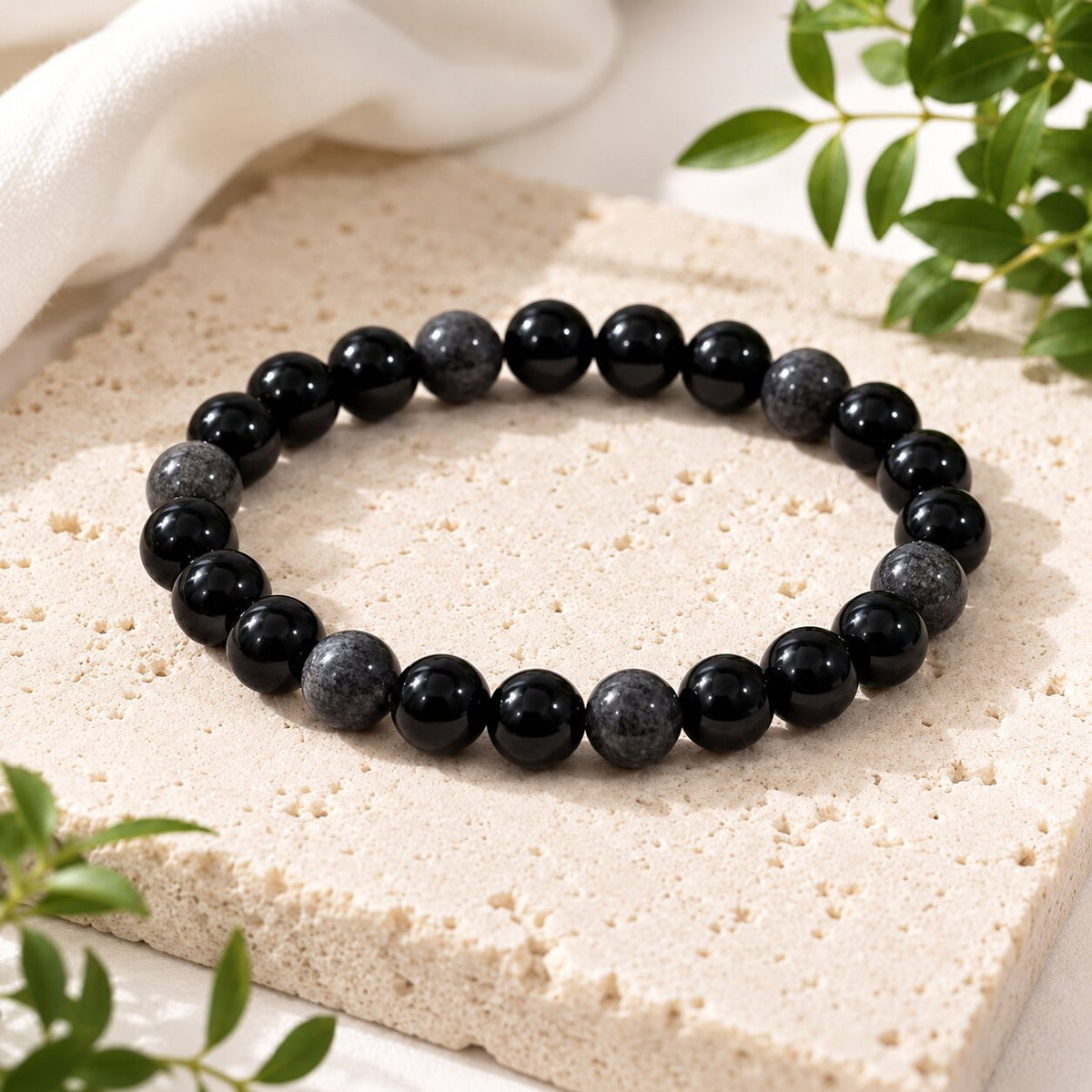 A beaded stretch bracelet made of alternating glossy black and mottled dark gray round beads