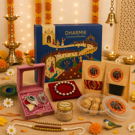 A festive Diwali gift set styled on a beige surface with warm string lights, marigold garlands, brass lamps, and a blue 'DHARMIK' box. The set includes a pink velvet box with silver jewelry, a beaded bracelet, packaged snacks, and a small jar, arranged decoratively with flowers and traditional props.