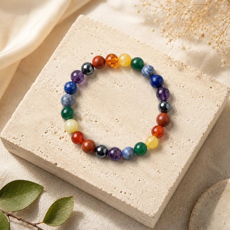 7 Chakra bracelet on a beige stone surface with leaves in the background