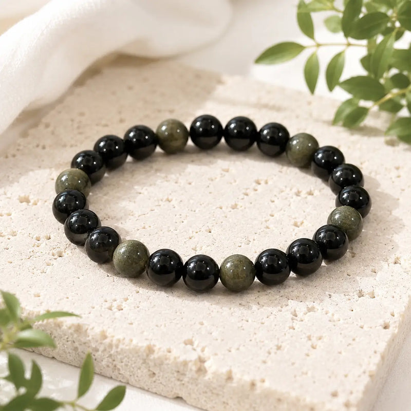 Beaded black obsidian bracelet  on a light stone surface with green leaves in the background