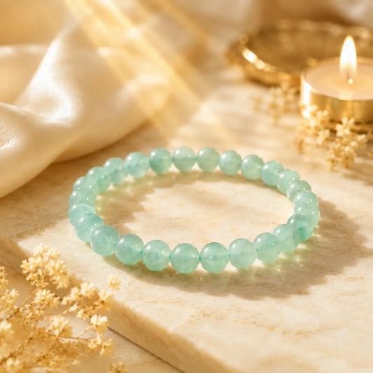 Green aventurine beaded bracelet on a wooden surface with gold coins and candle in the background