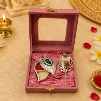 remium silver-plated tilak set in a pink gift box featuring a kumkum and akshat holder with a decorative peacock feather tilak applicator for pooja rituals.