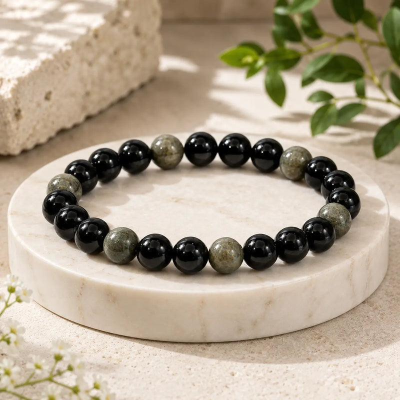 Black obsidian beaded bracelet on a marble stand with natural light and greenery in the background