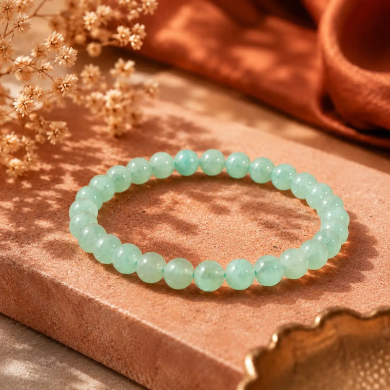 Green aventurine beaded bracelet on a wooden surface with dried flowers and a terracotta pot in the background.