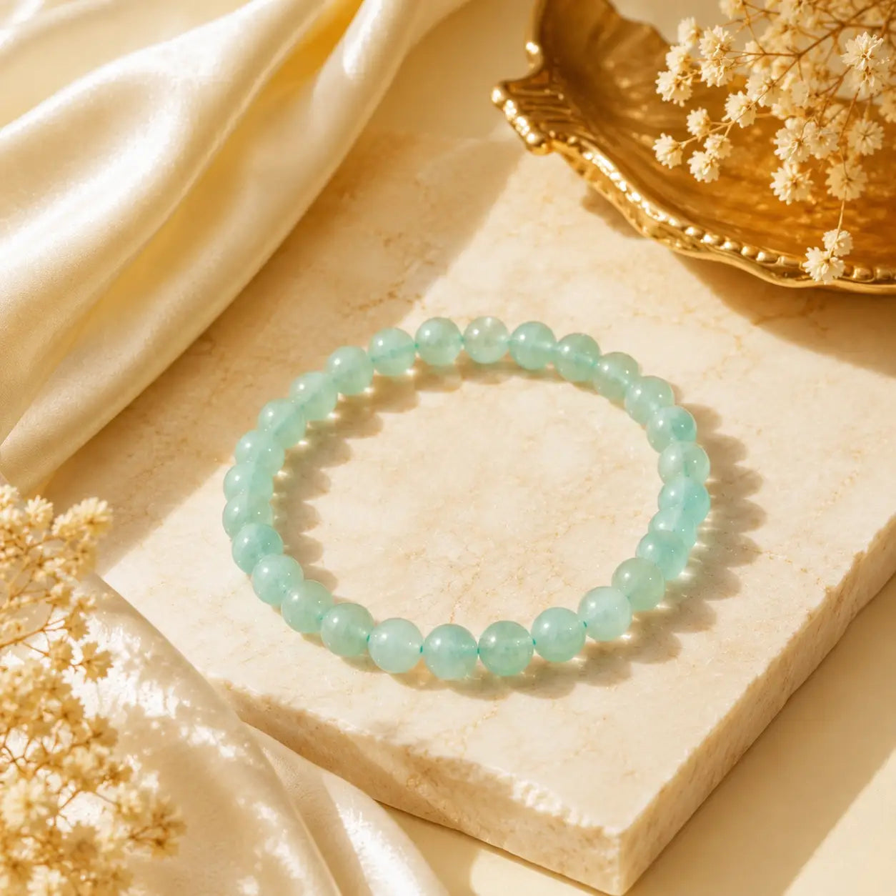 green aventurine  beaded bracelet on a beige stone surface with dried flowers and a gold dish.