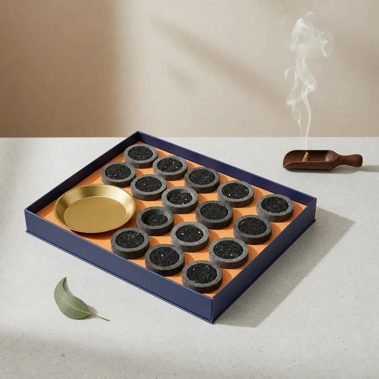 Set of incense cones in a box with a gold dish on a light surface.