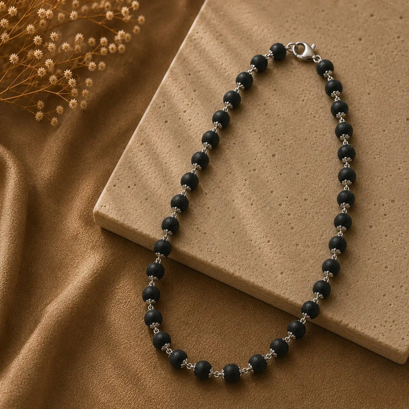 Karungali necklace on a beige stone surface with dried flowers.