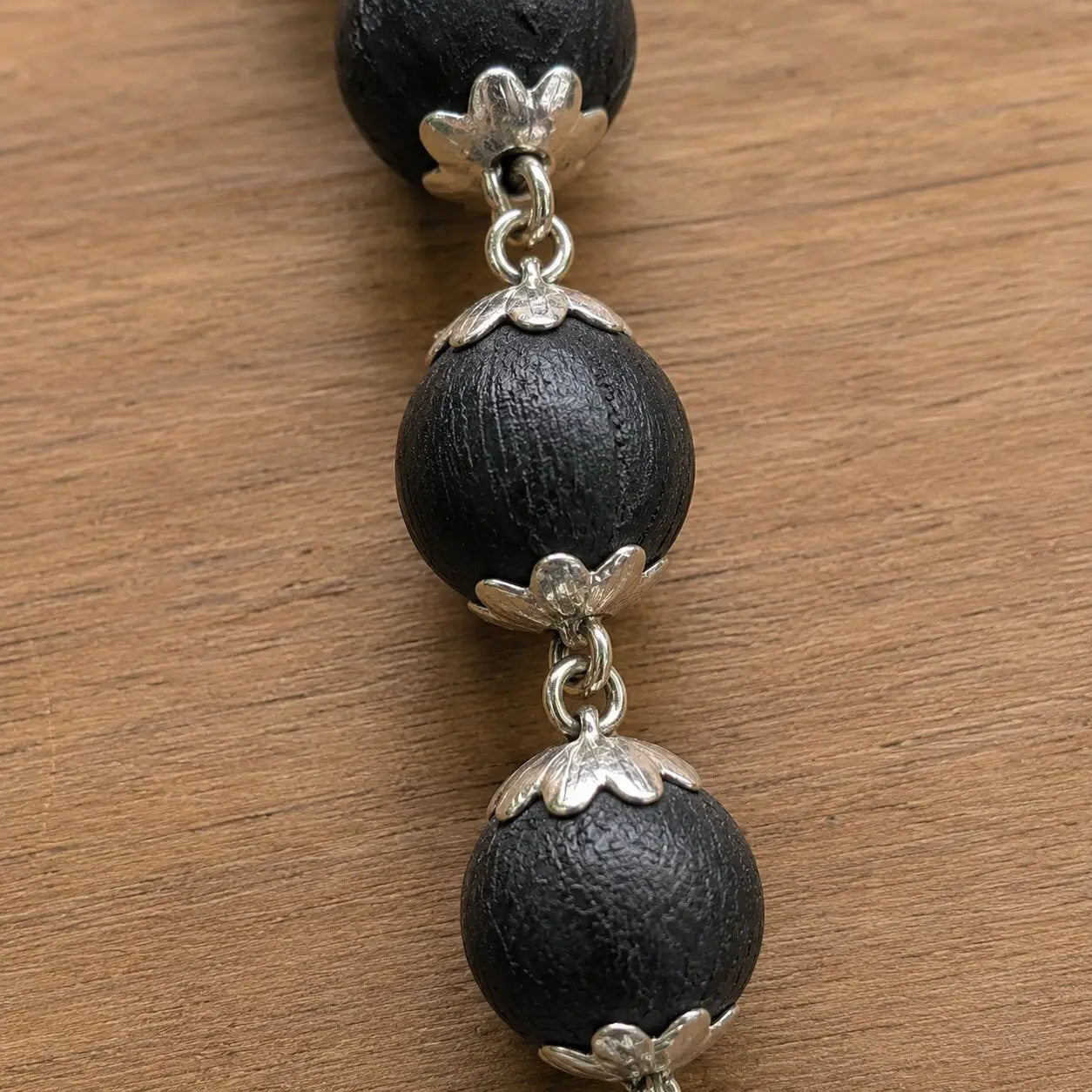 Karungali necklace with silver floral clasps on a wooden surface