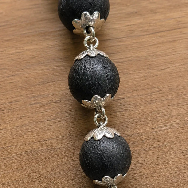 Karungali necklace with silver floral clasps on a wooden surface